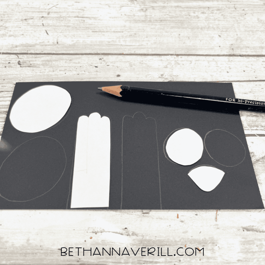 Panda face and body parts traced onto black construction paper with pencil.