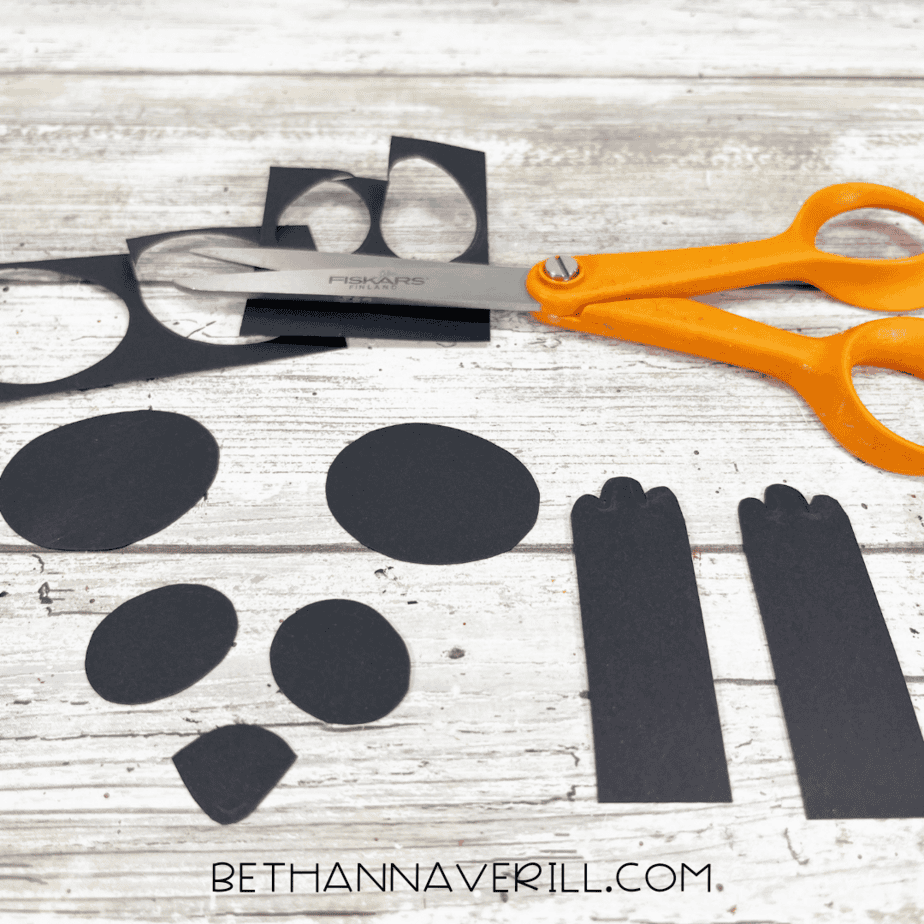 Black construction paper shapes for panda ears, arms, and eye patches cut out with scissors.