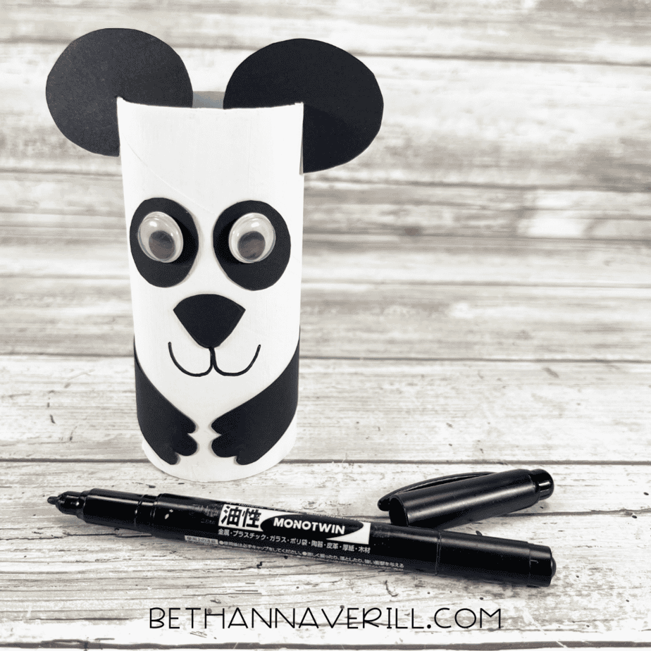 Panda craft with black marker drawing a smile on the white painted roll.