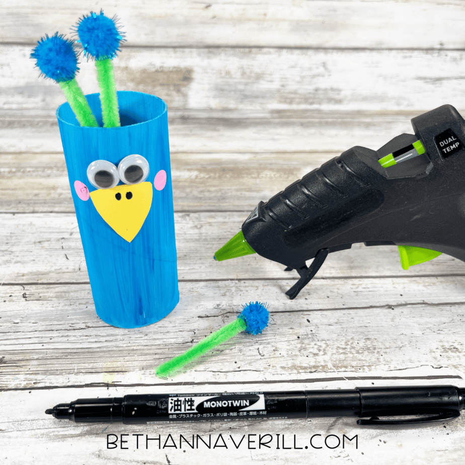 Toilet paper roll with googly eyes, beak, and feather toppers added.