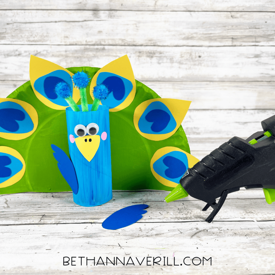 Toilet paper roll glued in front of decorated plate feathers with one wing attached.