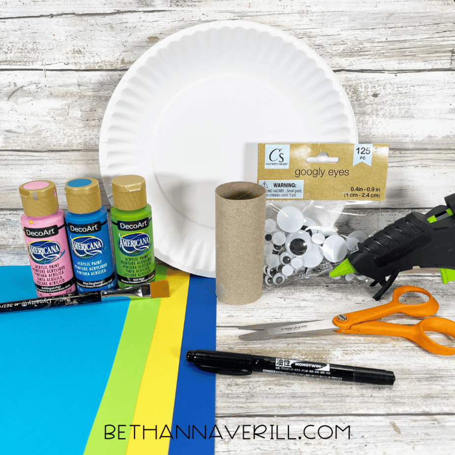 Materials for peacock paper roll craft including paint, toilet paper roll, paper plate, googly eyes, and construction paper.