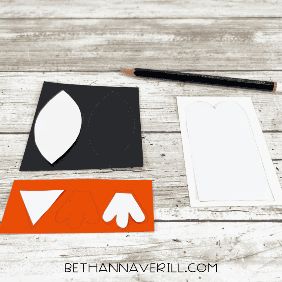 Paper templates for penguin body parts traced onto black, white, and orange construction paper.