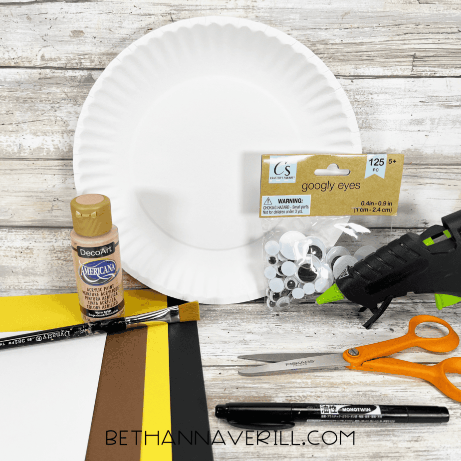 Materials for pirate boy paper plate craft including paint, googly eyes, glue gun, scissors, and paper.