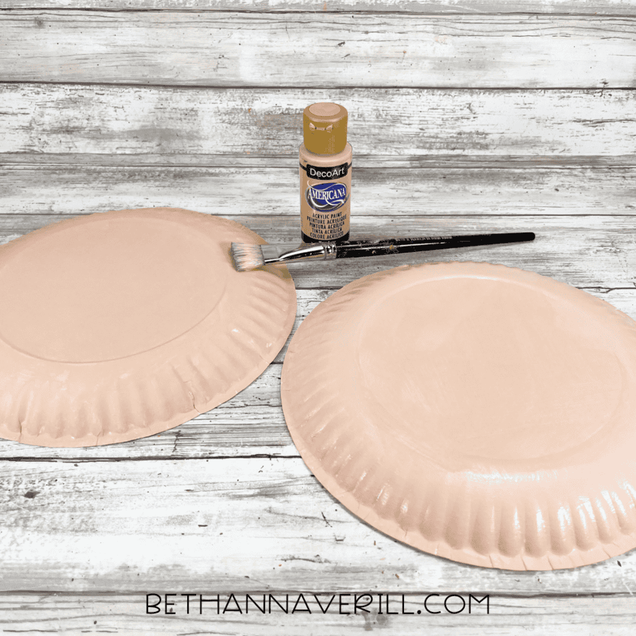 Paper plate painted light brown with acrylic paint and paintbrush beside it.