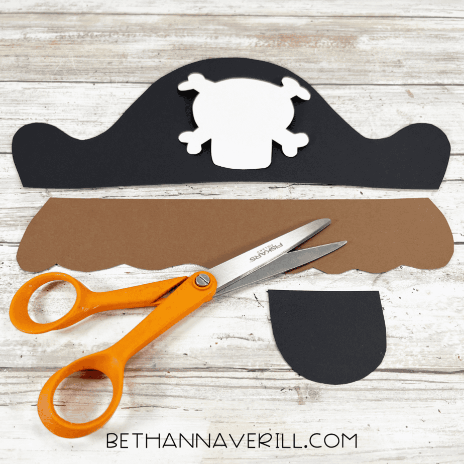 Cut-out pieces for pirate craft including black hat, white skull, brown hair, and eye patch.