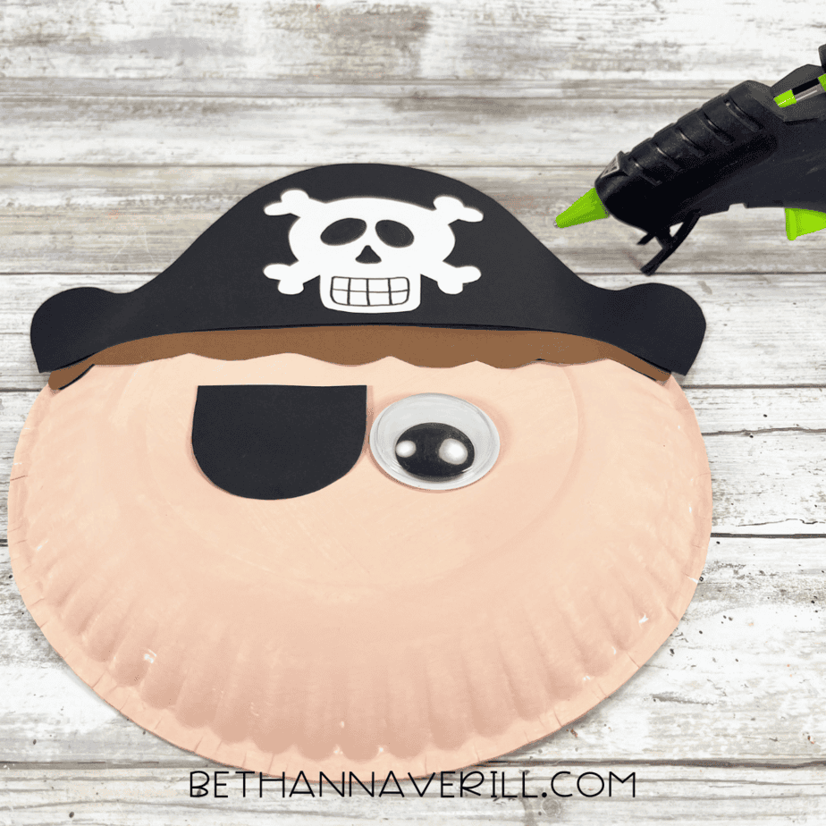 Paper plate pirate face with glued-on hair, hat, and one googly eye with eye patch.