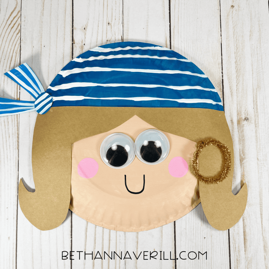 Finished pirate first mate girl paper plate craft with striped bandana, googly eyes, pink cheeks, and gold earring.