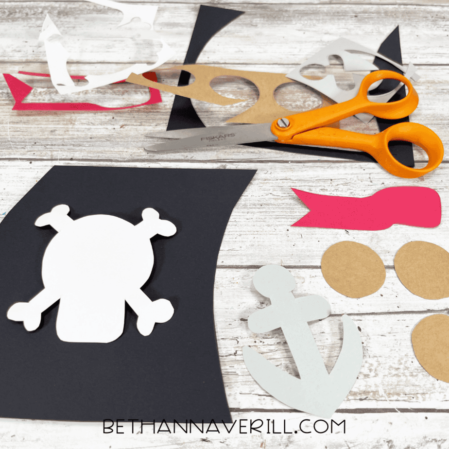 Cut out sail, anchor, flag, and window pieces for pirate ship craft.