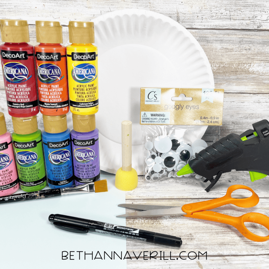 Rainbow paper plate craft materials including paint, googly eyes, paper plate, glue gun, and scissors.