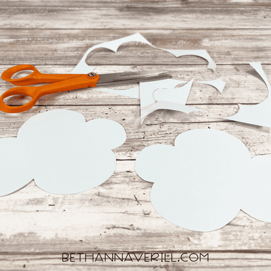 Cut-out white paper clouds on a wooden background.