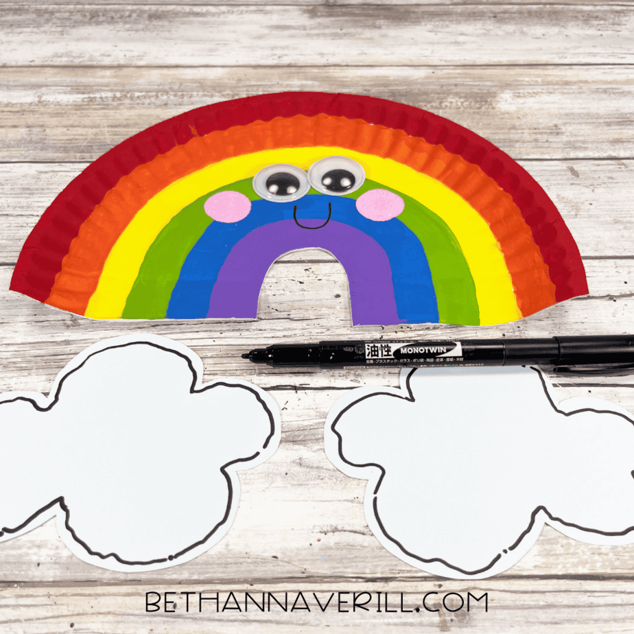 Rainbow paper plate with googly eyes and a smile drawn on, clouds cut out nearby.