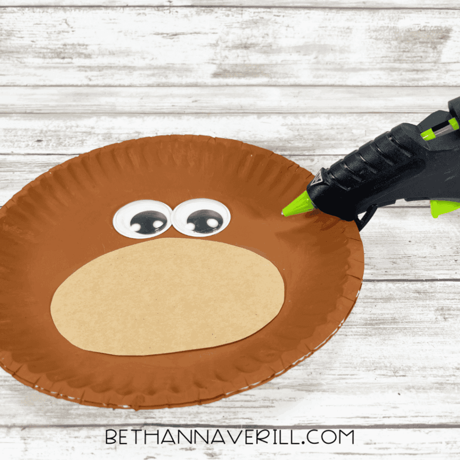 Brown paper plate with tan oval muzzle and large googly eyes glued on.