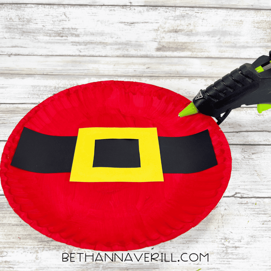 Black paper strip and yellow buckle glued onto red paper plate.