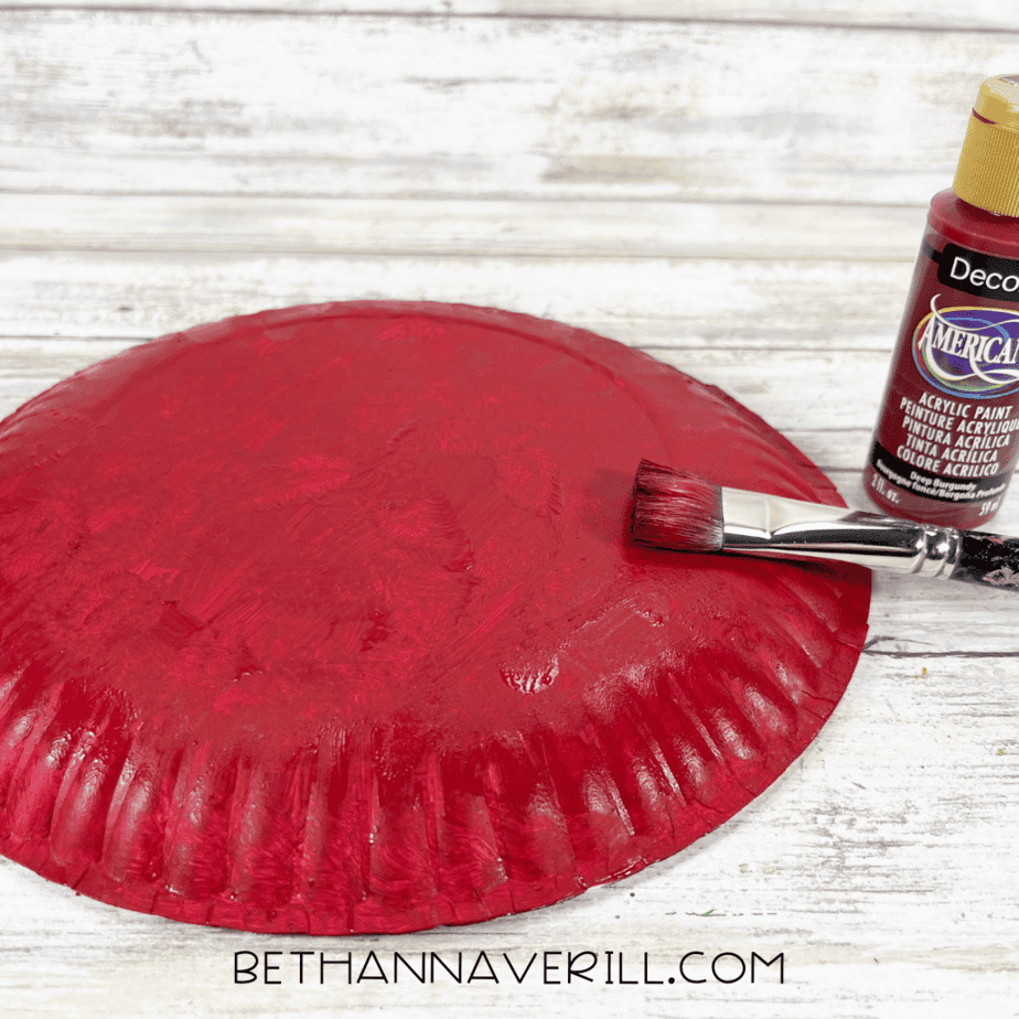 Paper plate painted red with acrylic paint and paintbrush.