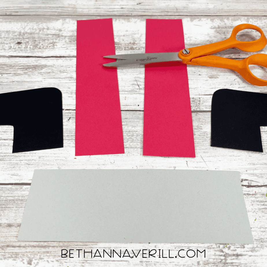 Cut-out pieces of red pant legs, black boots, and gray rectangle.