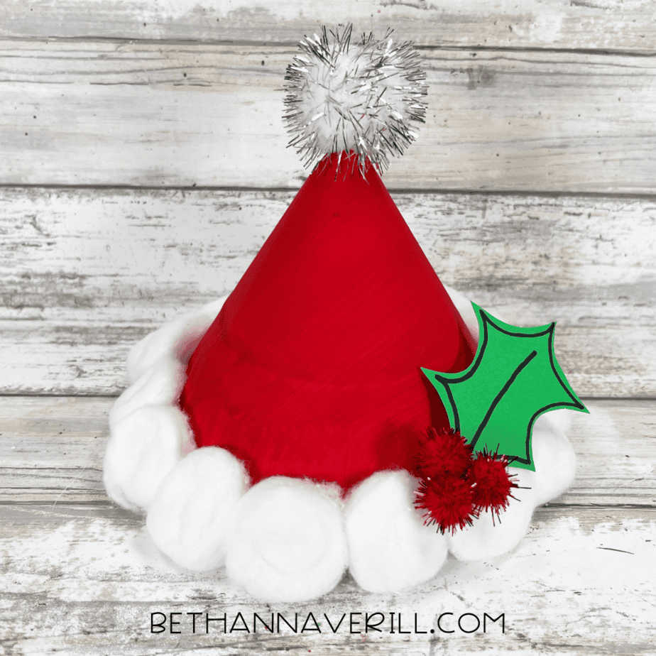 Finished Santa hat paper plate craft with fluffy trim and holly decoration.