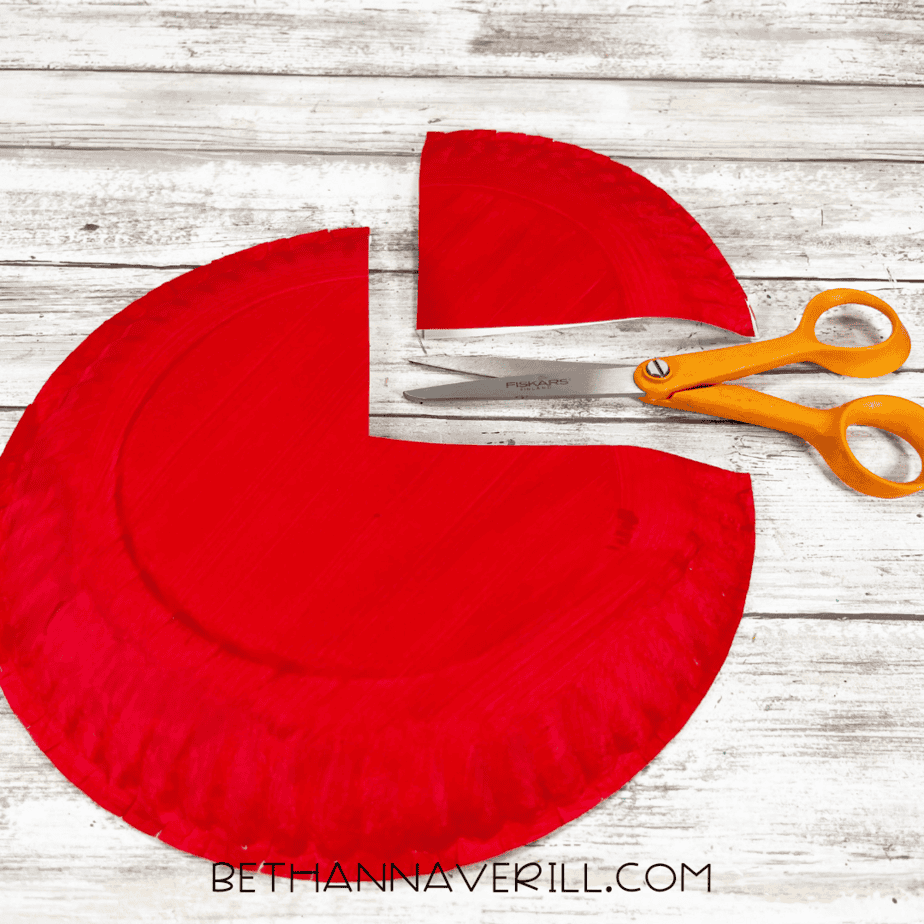 Red painted paper plate with a wedge cut out and scissors next to it.