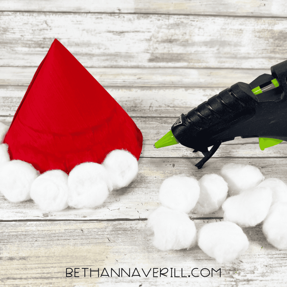 Cotton balls being glued around the base of the red paper plate hat.