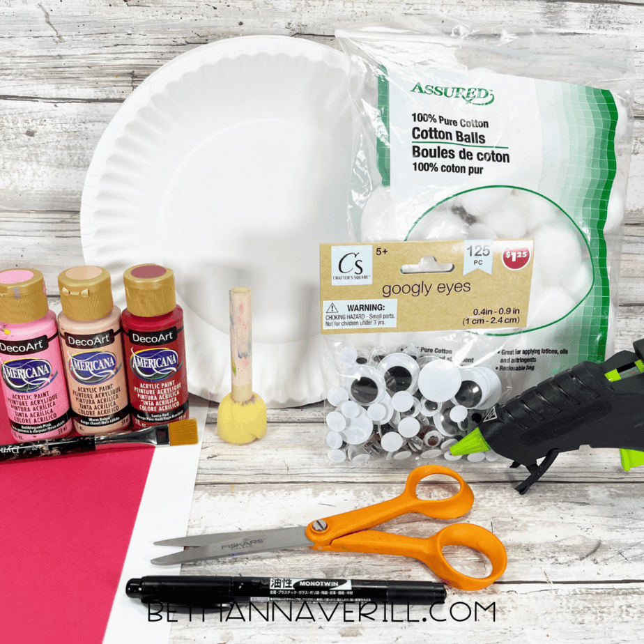 Craft supplies for Santa paper plate craft including paper plate, paint, construction paper, cotton balls, googly eyes, and glue gun.