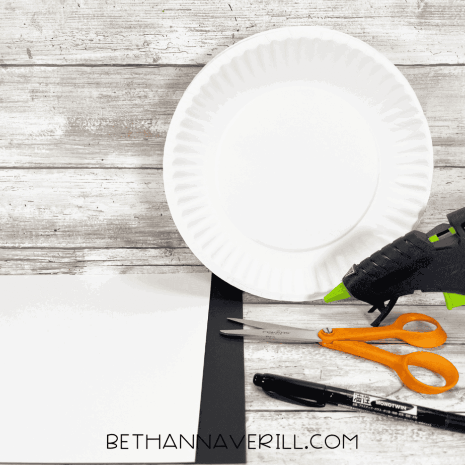 Paper plate skull craft supplies with scissors, glue, and construction paper.
