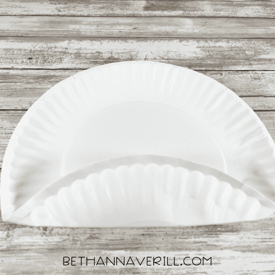 Paper plate folded in half to prepare for cutting.
