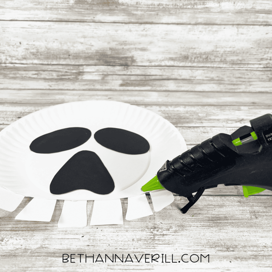 Adding white paper teeth pieces to the bottom of the paper plate skull.