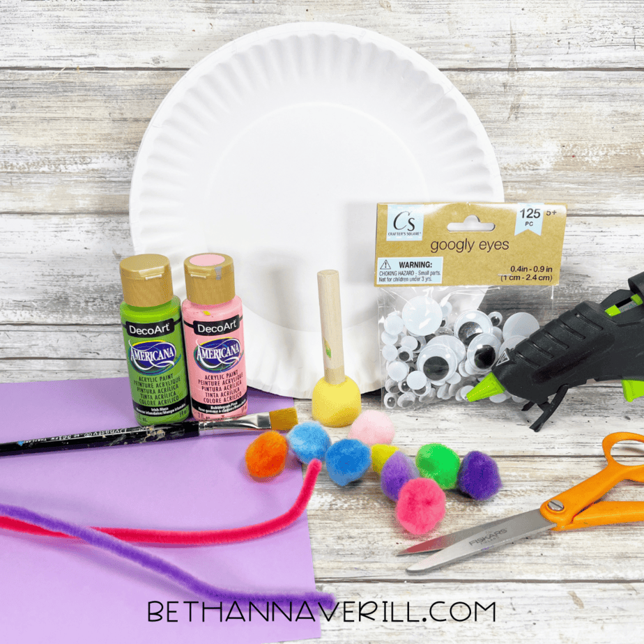 Paper plate snail craft supplies including paint, pom poms, googly eyes, pipe cleaners, and paper.