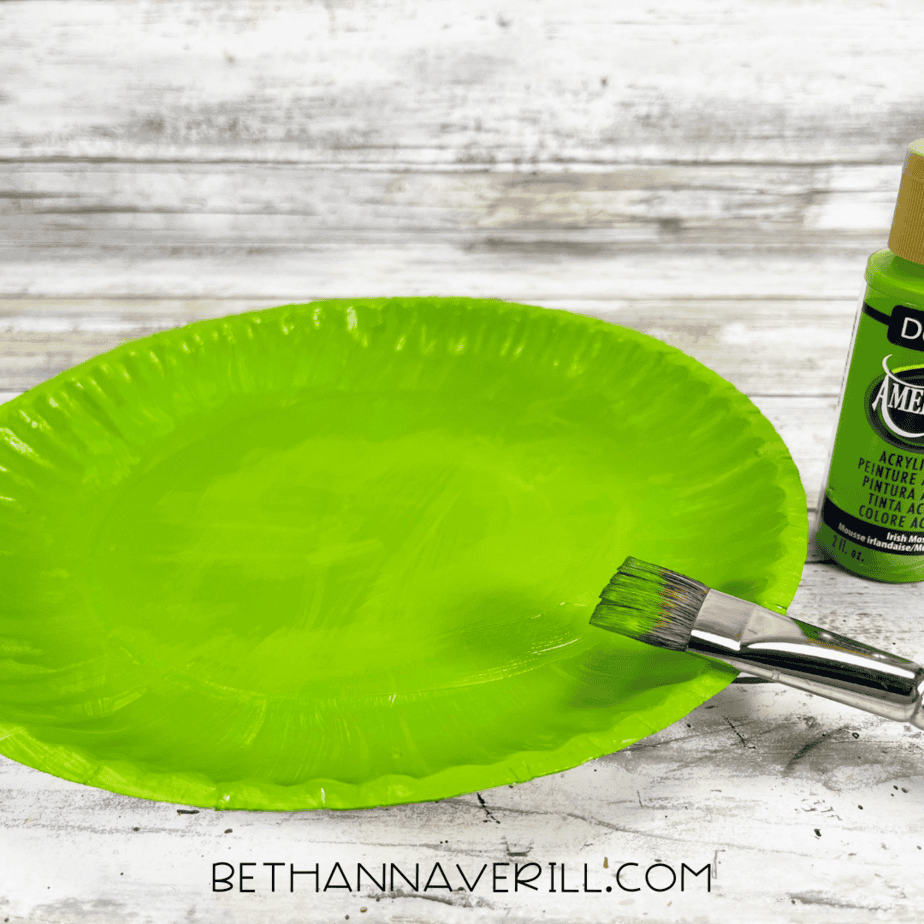 Paper plate painted green with a paintbrush beside it.