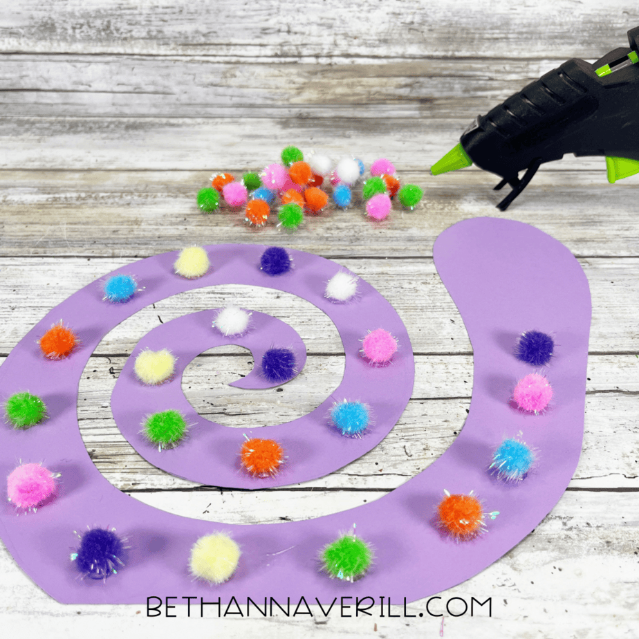 Colorful pom poms glued onto purple spiral shell.