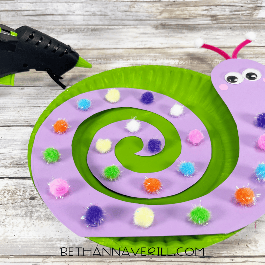 Purple snail shell with pom poms glued to green paper plate.