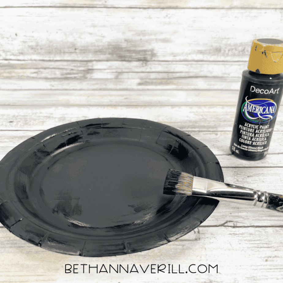 Paper plate painted black with a paintbrush and black paint beside it.