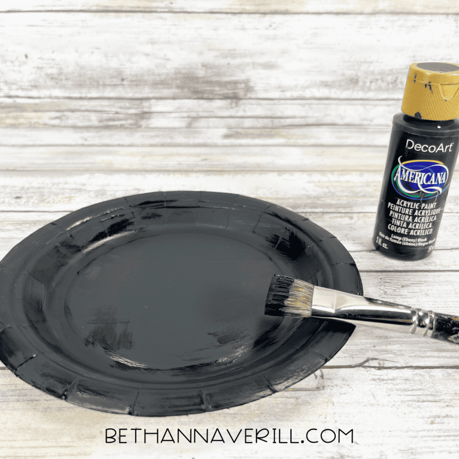 Paper plate painted black with a paintbrush and black paint beside it.