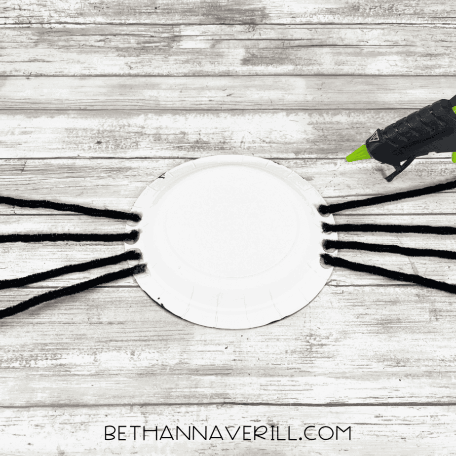 Back of black plate with pipe cleaners glued on for legs.