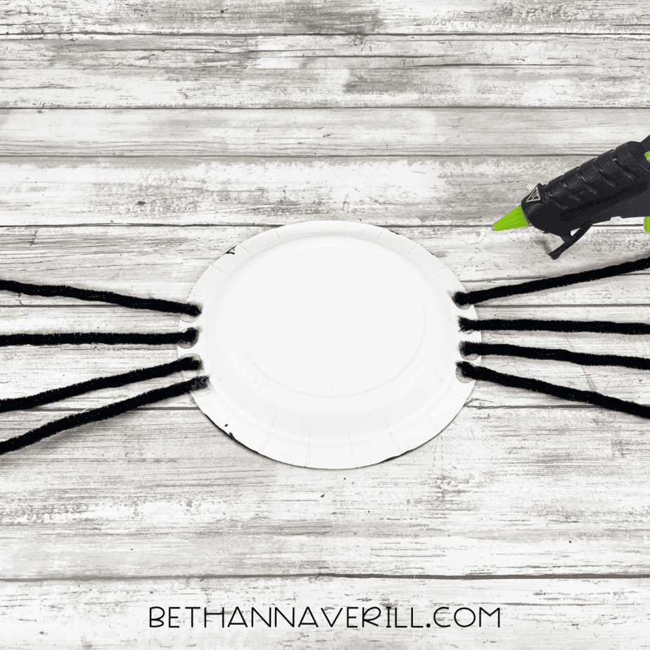 Back of black plate with pipe cleaners glued on for legs.