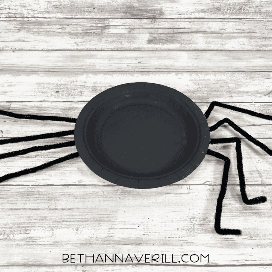 Black spider plate flipped over with bent pipe cleaner legs.
