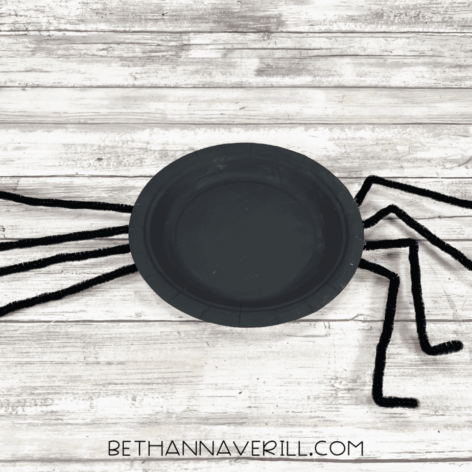 Black spider plate flipped over with bent pipe cleaner legs.