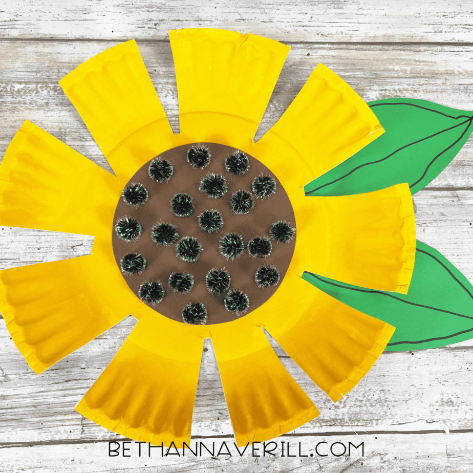 Finished sunflower craft with black pom-poms in the center and two green leaves attached.