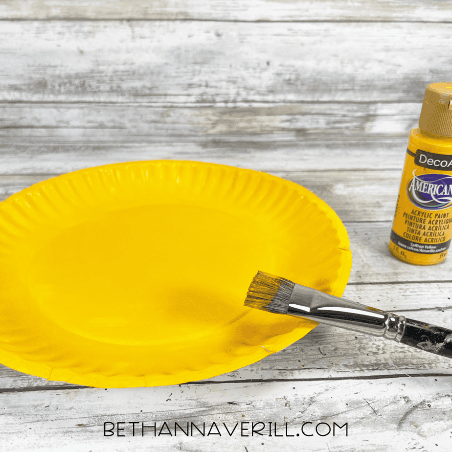 Paper plate painted bright yellow with a paintbrush and yellow paint beside it.