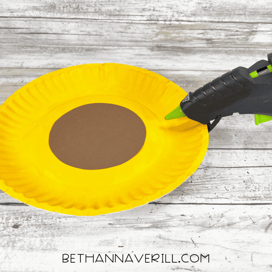 Yellow-painted paper plate with brown circle glued in the center using a glue gun.