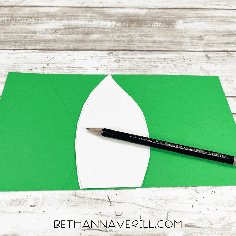 White leaf template traced onto green construction paper with a pencil.