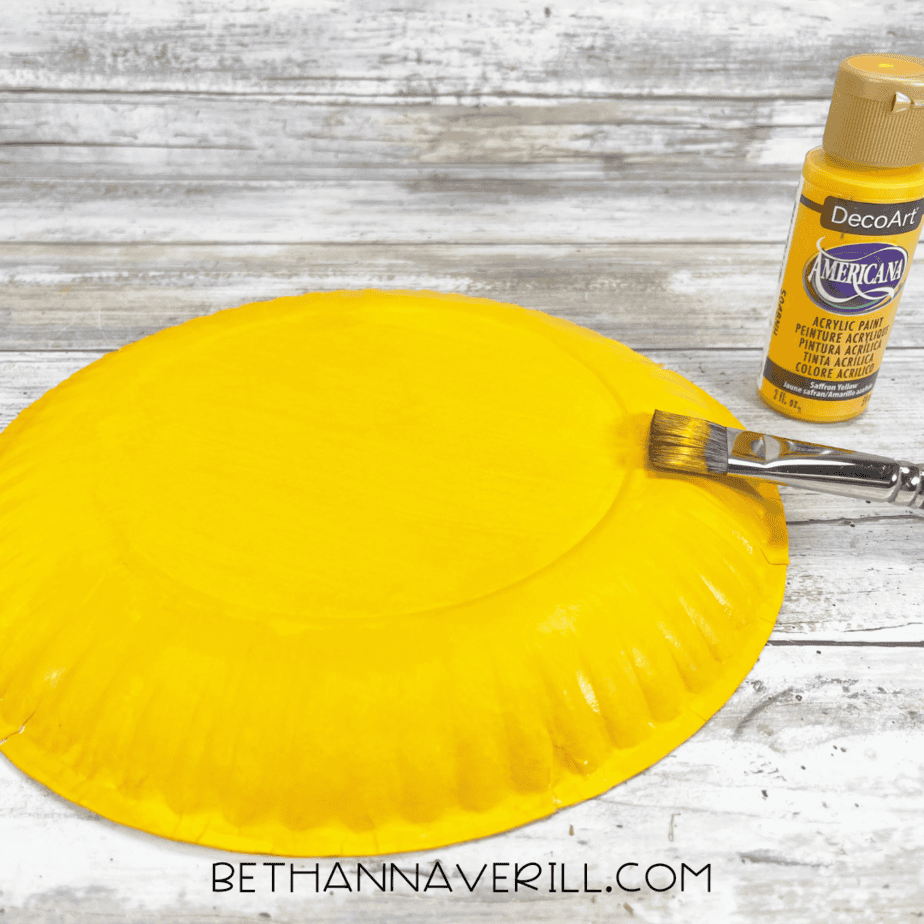 Paper plate painted bright yellow with a paintbrush and yellow paint beside it.