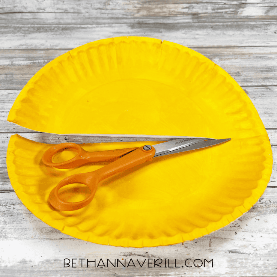 Yellow painted paper plate cut in half with scissors resting on top.