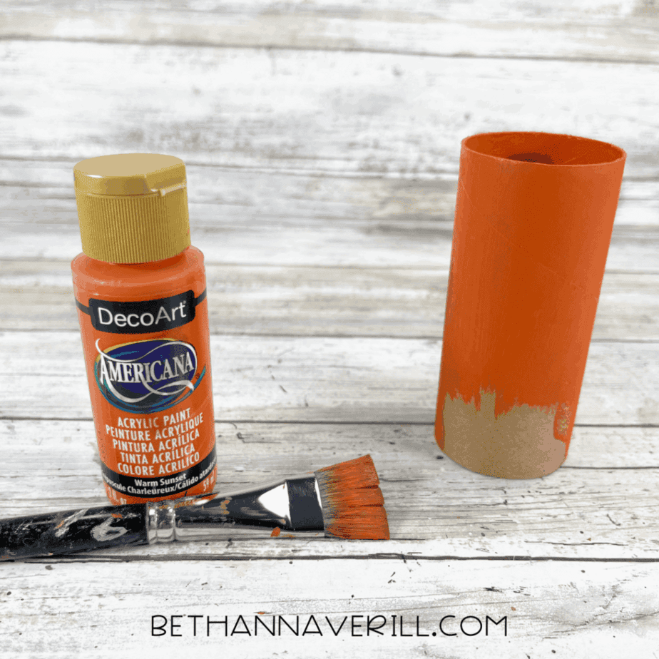 Cardboard toilet paper roll being painted orange with acrylic paint.