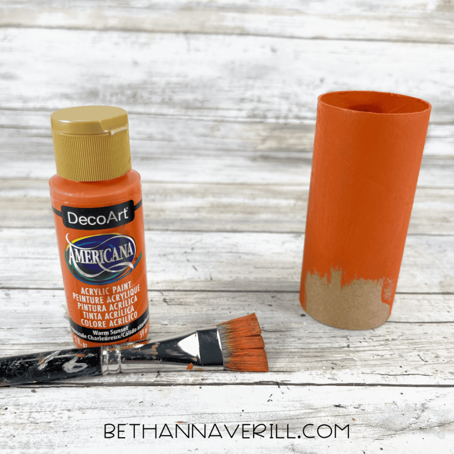 Cardboard toilet paper roll being painted orange with acrylic paint.