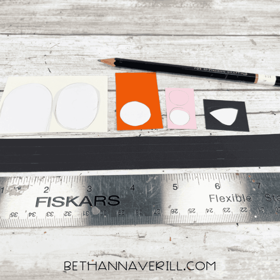 Pencil tracing circle and oval shapes onto orange, pink, black, and white paper with a ruler nearby.