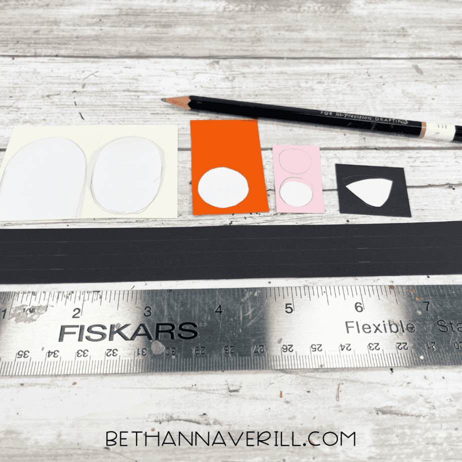 Pencil tracing circle and oval shapes onto orange, pink, black, and white paper with a ruler nearby.