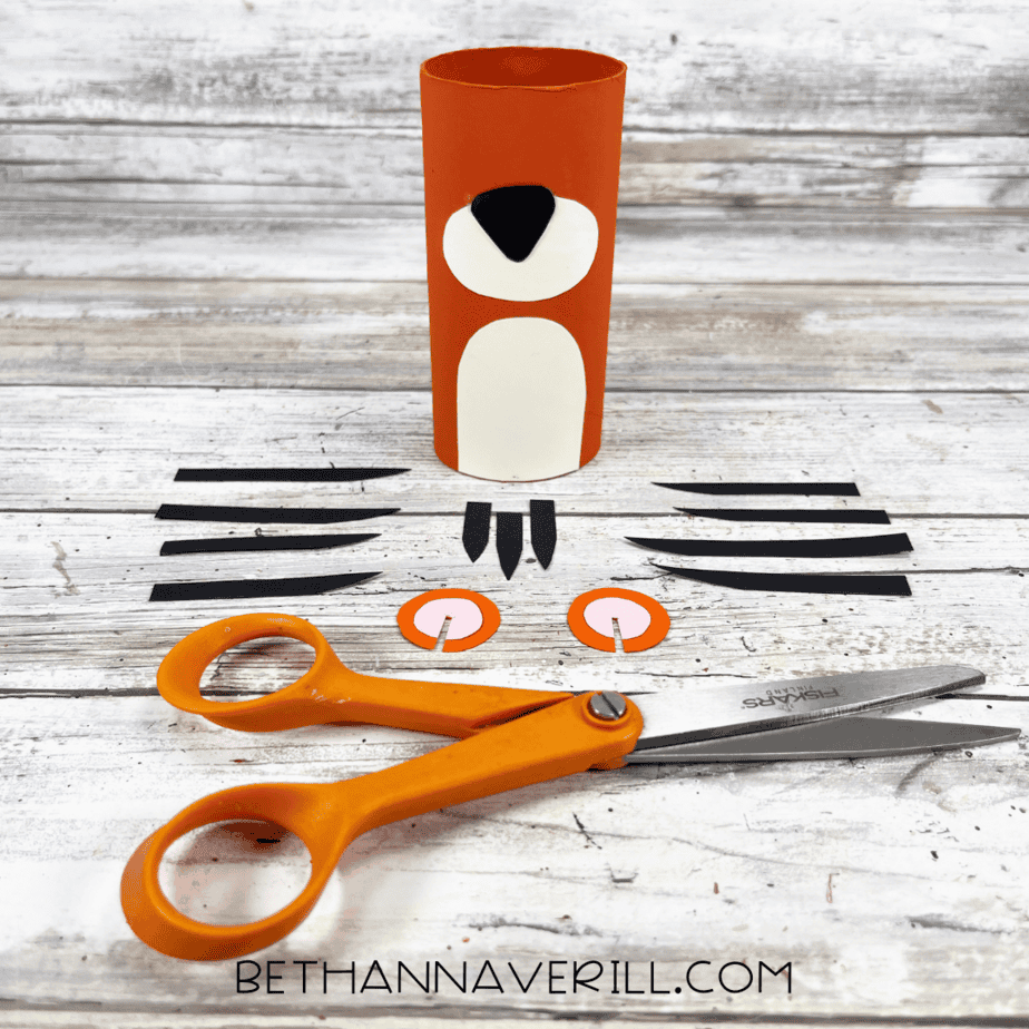 Orange painted paper roll with white belly and muzzle glued on, surrounded by cut stripes, ears, and other pieces.