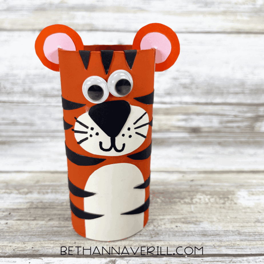Finished tiger paper roll craft standing upright with googly eyes, ears, and black stripes.