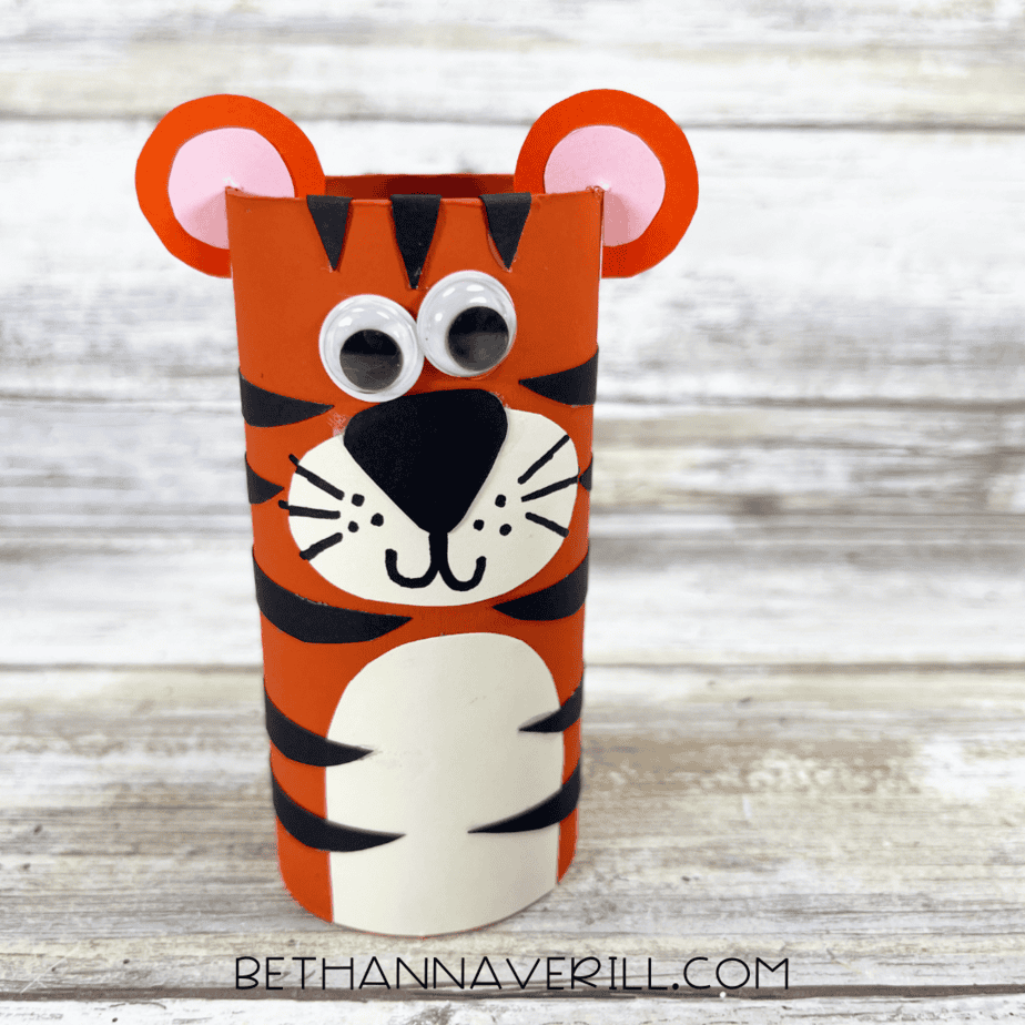Finished tiger paper roll craft standing upright with googly eyes, ears, and black stripes.
